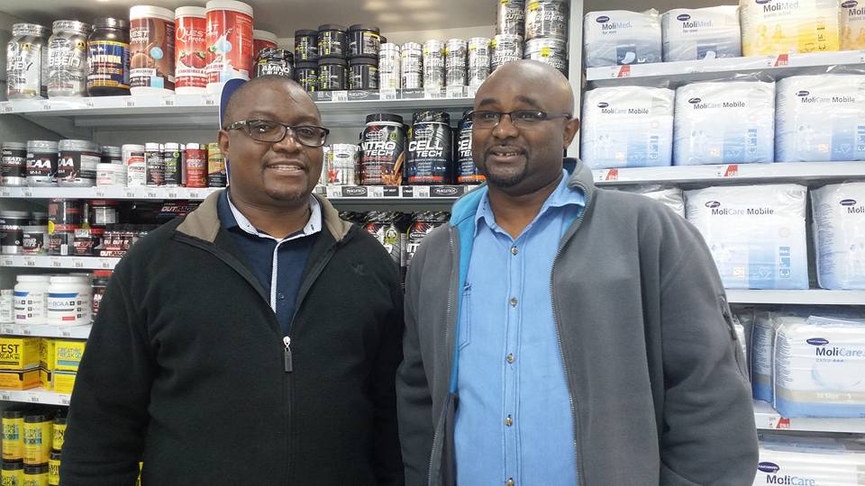 Pharmacists | Messages From Heroes Two men are seen inside a retail store stocked with health products and supplements, highlighting service from frontline.